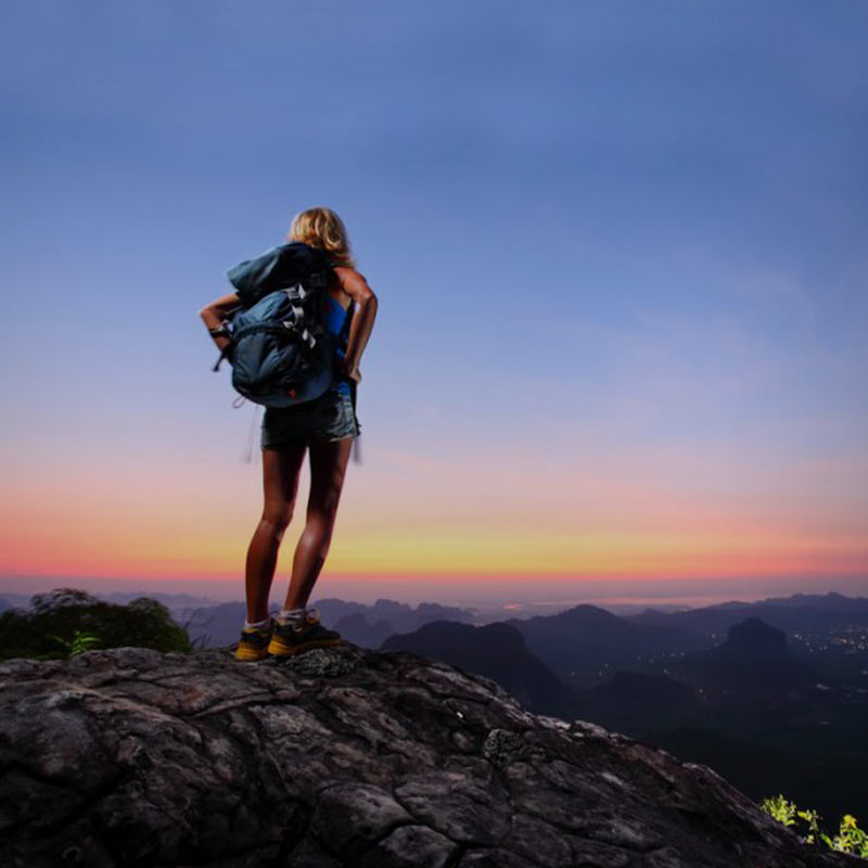 Woman standing with backpack on mountain.  She is meant to symbolize an outdoor survival or camping gear enthusiast.  It's assumed she would be carrying PrimalCamp hand crank solar powered flashlights in her backpack.