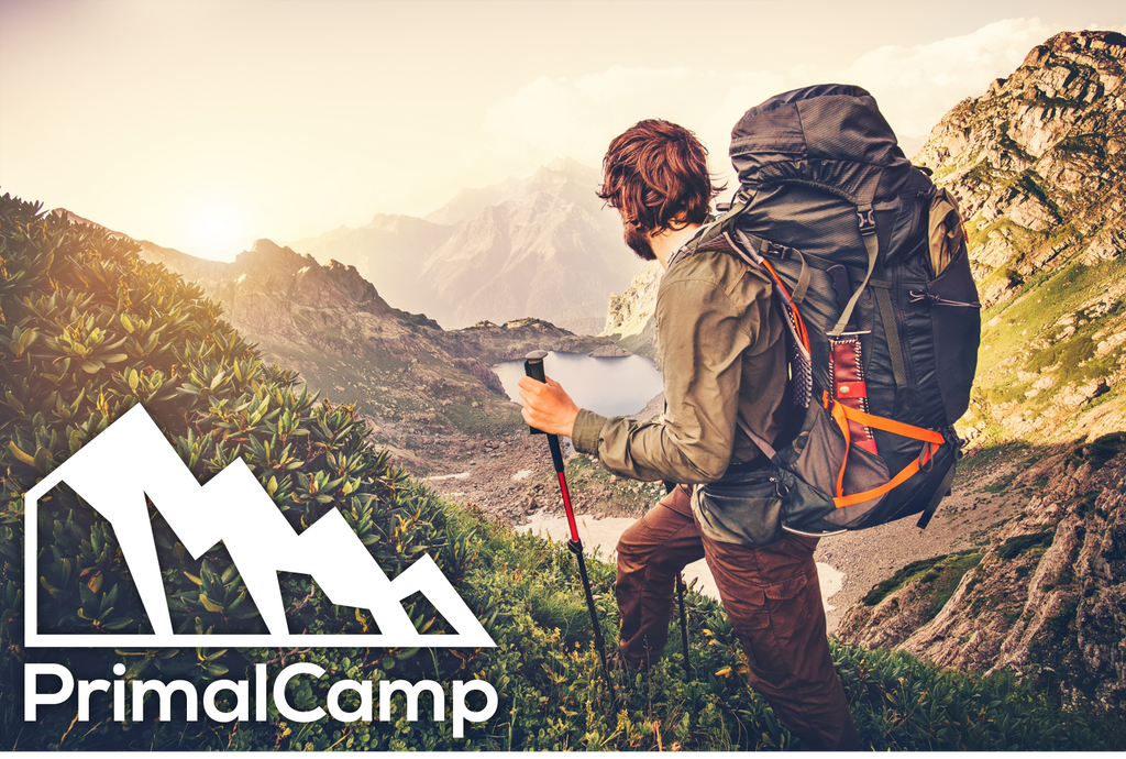 PrimalCamp logo for their solar hand crank flashlights next to a man with hiking backpack and survival gear.  He is on top of a mountain and likely camping.